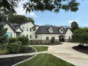 View of front facade featuring stone siding, stucco siding, curved driveway, and a front lawn