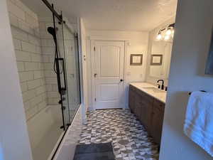 Full bath with enclosed tub / shower combo, vanity, a textured ceiling, and tile patterned floors
