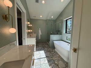 Primary bathroom with 2 vanities, vaulted ceiling, a freestanding bath, a shower stall, and marble flooring