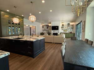 Kitchen with dark wood-style flooring, recessed lighting, dark cabinetry, light stone countertops, and decorative light fixtures
