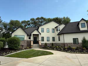 View of front facade featuring stucco siding, stone siding, a front lawn, and roof with shingles
