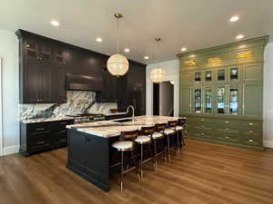 Kitchen featuring backsplash, dark wood-style flooring, a breakfast bar area, light stone counters, and recessed lighting