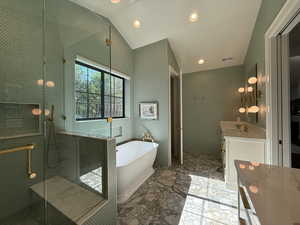 Primary bathroom with 2 vanities, vaulted ceiling, a freestanding bath, a shower stall, and marble flooring