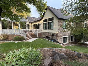 View of front of property with stone siding, stucco siding, roof with shingles, a front yard, and a deck