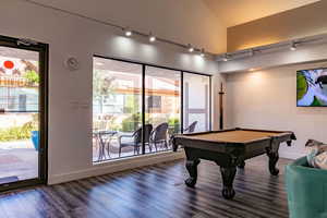 Rec room featuring healthy amount of natural light, billiards table, wood finished floors, vaulted ceiling, and a textured wall