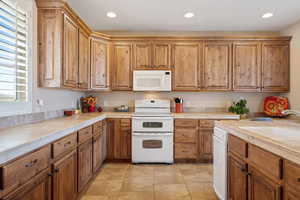 Kitchen featuring white appliances, recessed lighting, brown cabinetry, light tile patterned floors, and tile countertops