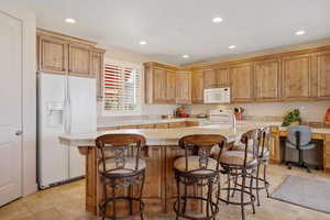 Kitchen featuring white appliances, light countertops, a center island with sink, recessed lighting, and a kitchen breakfast bar