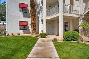 View of exterior entry with stucco siding, a yard, and a balcony