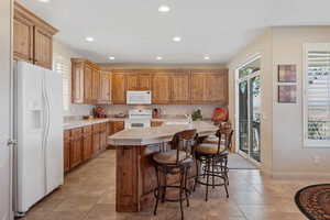 Kitchen featuring white appliances, light countertops, recessed lighting, light tile patterned floors, and a kitchen island with sink