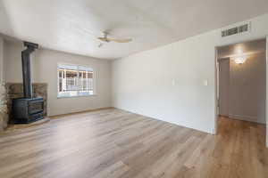 Unfurnished living room featuring a ceiling fan, a wood stove, and light wood-type flooring