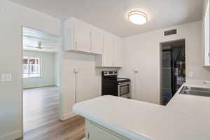 Kitchen with stainless steel electric range oven, light wood finished floors, white cabinets, a peninsula, and light countertops