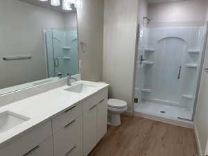Full bath featuring wood finished floors, a shower stall, and double vanity