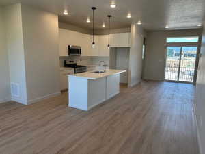 Kitchen featuring appliances with stainless steel finishes, white cabinetry, backsplash, light wood-style floors, and light countertops