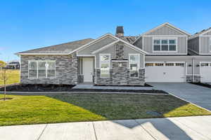 Craftsman house with stone siding, concrete driveway, a front lawn, and board and batten siding