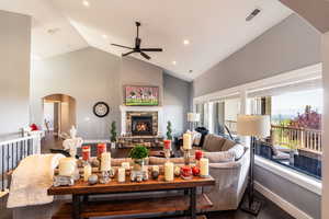 Living room with arched walkways, dark wood-style flooring, a ceiling fan, a fireplace, and high vaulted ceiling