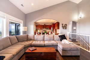 Living area featuring high vaulted ceiling, dark wood-style floors, arched walkways, and recessed lighting