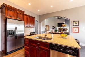 Kitchen featuring arched walkways, stainless steel appliances, dark brown cabinets, dark wood-style floors, and a ceiling fan