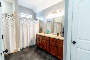 Bathroom featuring vaulted ceiling, double vanity, and a shower with shower curtain