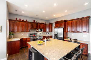 Kitchen with appliances with stainless steel finishes, dark wood-style floors, an island with sink, decorative backsplash, and recessed lighting