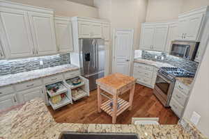 Kitchen with high quality appliances, tasteful backsplash, white cabinetry, wood finished floors, and light stone counters