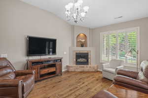 Living room featuring a chandelier, vaulted ceiling, a tile fireplace, and light wood finished floors