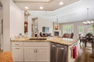Kitchen featuring a chandelier, dishwasher, open floor plan, light stone counters, and a tile fireplace