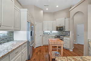 Kitchen featuring stainless steel appliances, wood-type flooring, backsplash, white cabinetry, and recessed lighting