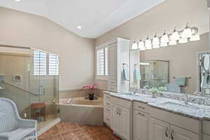 Bathroom featuring double vanity, a garden tub, a stall shower, lofted ceiling, and tile patterned flooring