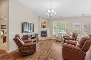 Living area with light wood-style floors, a chandelier, lofted ceiling, and a tiled fireplace
