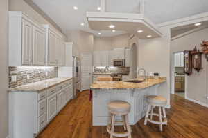 Kitchen with a peninsula, a breakfast bar, dark wood-type flooring, light stone counters, and recessed lighting