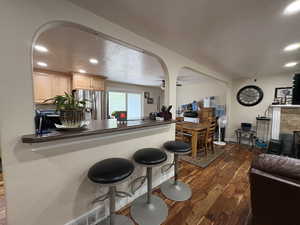 Kitchen with dark wood-style flooring, stainless steel fridge, dark countertops, a textured ceiling, and recessed lighting
