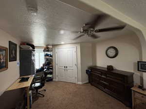 Carpeted office space with a textured ceiling and ceiling fan