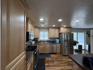Kitchen with stainless steel appliances, light brown cabinets, dark wood-style flooring, a textured ceiling, and recessed lighting