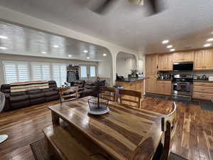 Dining area featuring a textured ceiling, arched walkways, recessed lighting, and dark wood-style floors