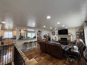 Living room with a textured ceiling, a ceiling fan, dark wood-type flooring, a fireplace, and recessed lighting