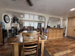 Dining space with dark wood-style flooring, a textured ceiling, recessed lighting, and arched walkways