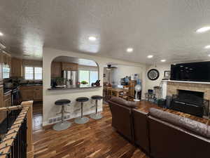 Living area featuring a textured ceiling, dark wood-style flooring, a fireplace, ceiling fan, and recessed lighting