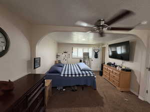 Bedroom featuring light carpet, a textured ceiling, ceiling fan, and arched walkways