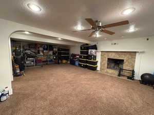 Carpeted living area featuring a textured ceiling, ceiling fan, a fireplace, and recessed lighting