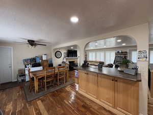 Dining space featuring a textured ceiling, a ceiling fan, a fireplace, dark wood finished floors, and arched walkways