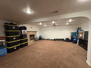 Playroom featuring carpet floors, a textured ceiling, a tiled fireplace, and ceiling fan