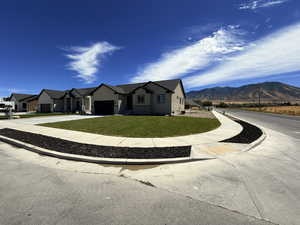 View of front facade featuring stucco siding, concrete driveway, a front lawn, stone siding, and an attached garage