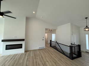 Unfurnished living room with wood finished floors, a glass covered fireplace, ceiling fan, high vaulted ceiling, and recessed lighting