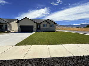 View of front of home featuring stucco siding, stone siding, a front yard, concrete driveway, and an attached garage