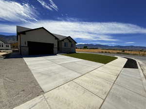View of property exterior with a mountain view, driveway, a garage, a yard, and stone siding