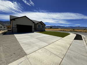 View of front of house featuring a mountain view, driveway, an attached garage, a front lawn, and stucco siding