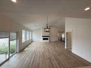 Unfurnished living room featuring vaulted ceiling, light wood-style flooring, a fireplace, and recessed lighting