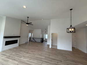 Unfurnished living room featuring high vaulted ceiling, light wood finished floors, a fireplace, a chandelier, and ceiling fan