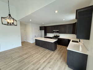 Kitchen with stainless steel appliances, light wood finished floors, a center island, a chandelier, and light countertops