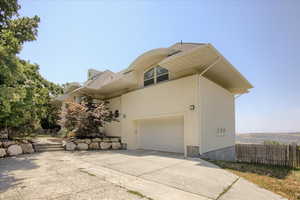 View of side of home with concrete driveway, a shingled roof, an attached garage, and stucco siding